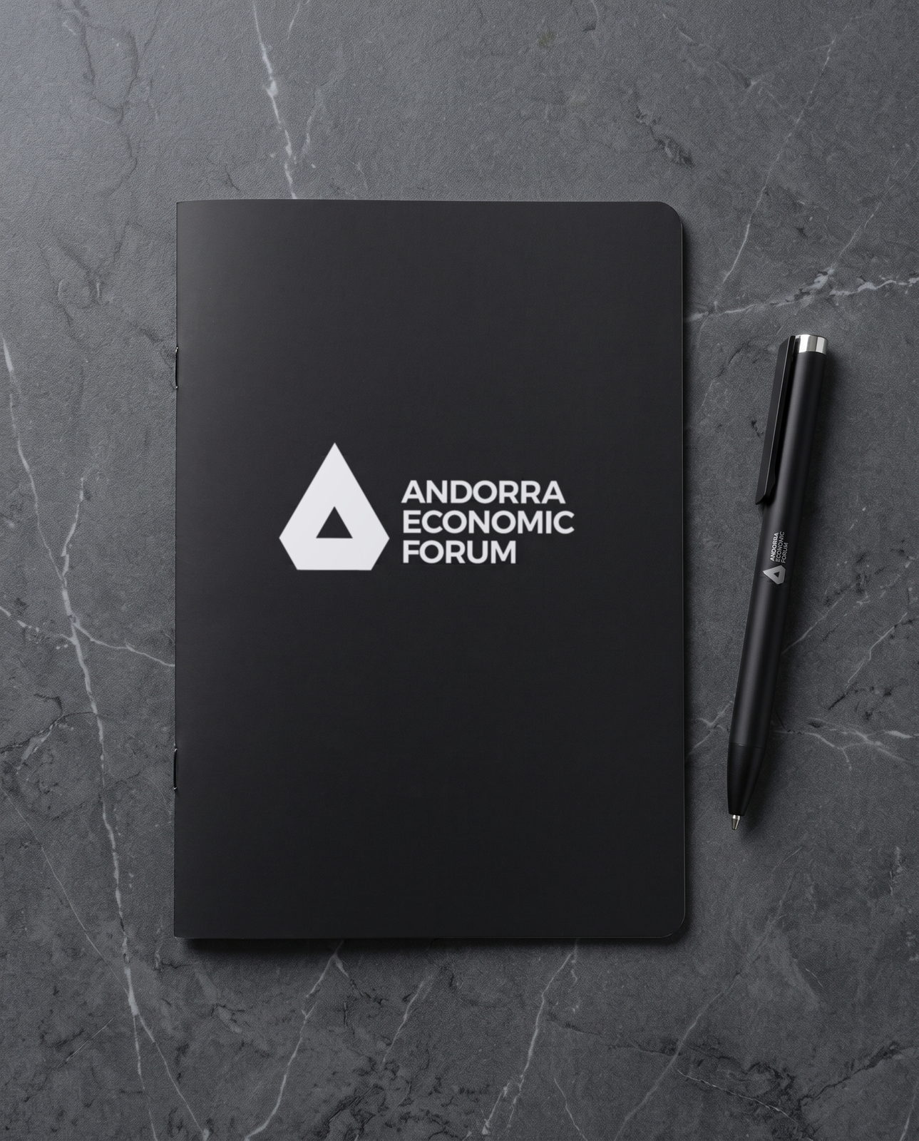 Libreta A5 de tapa negra con el logotipo del Andorra Economic Forum impreso en blanco, junto al bolígrafo de aluminio negro a juego